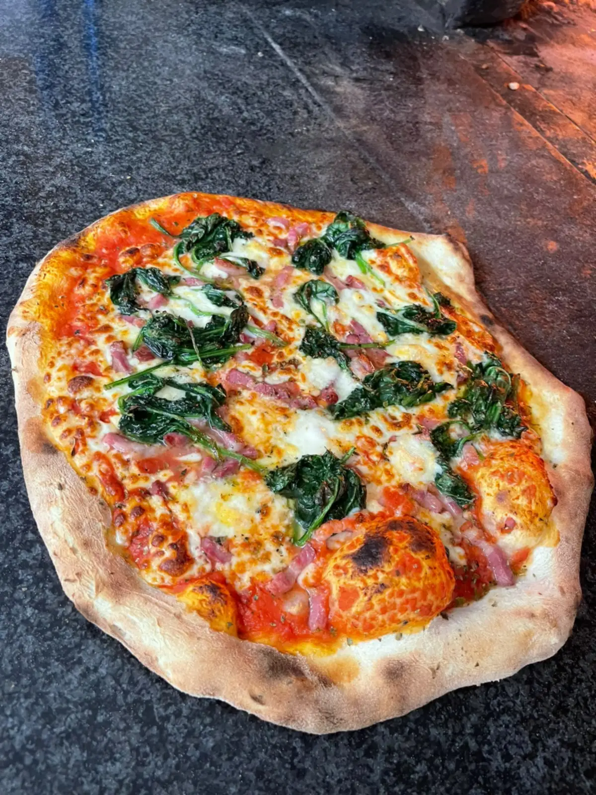 Une pizza aux épinards et lardons à la sortie du four à bois.