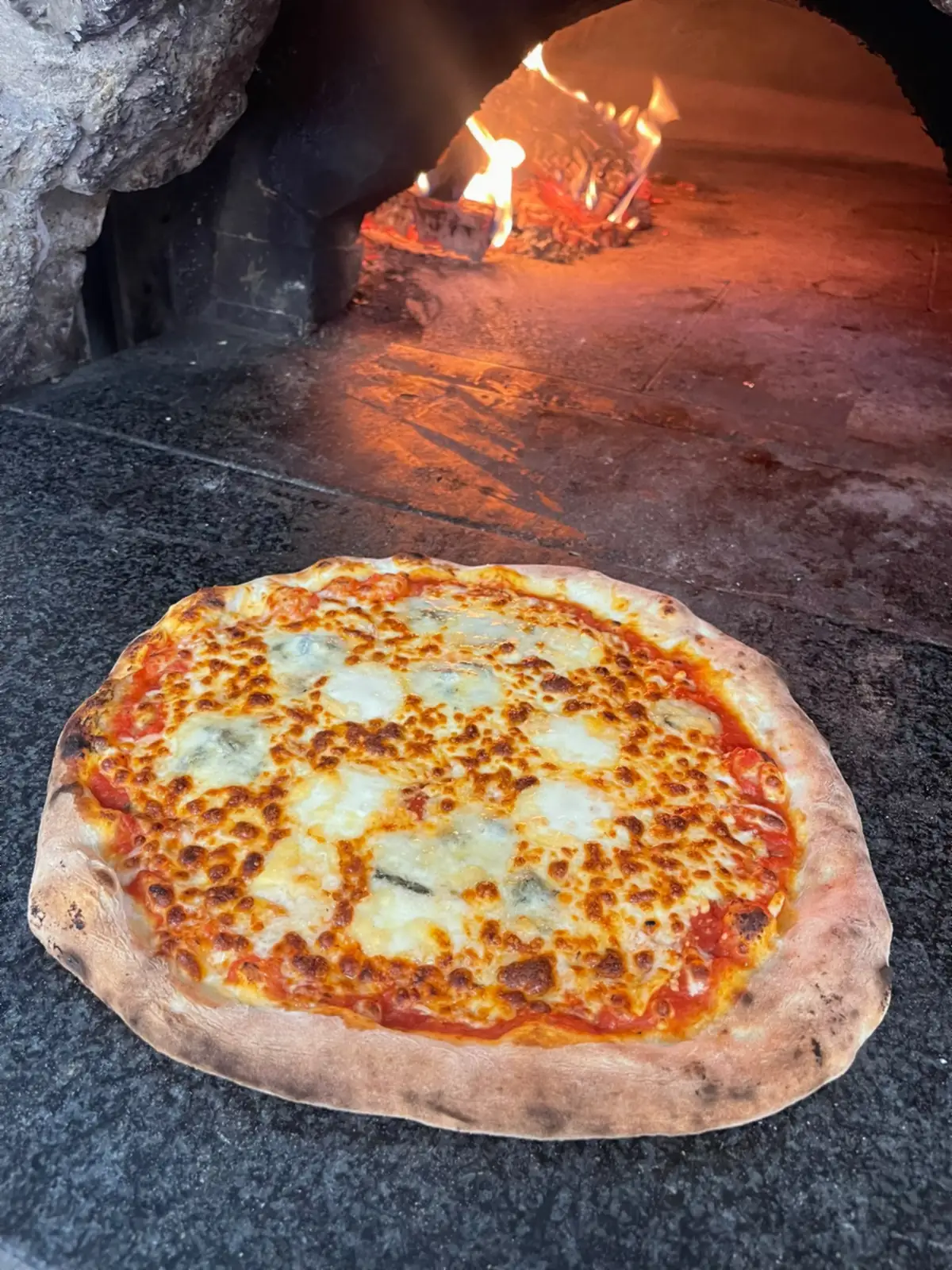 Le bord d’une pizza aux fromages, gonflé et marqué par la cuisson au bois.