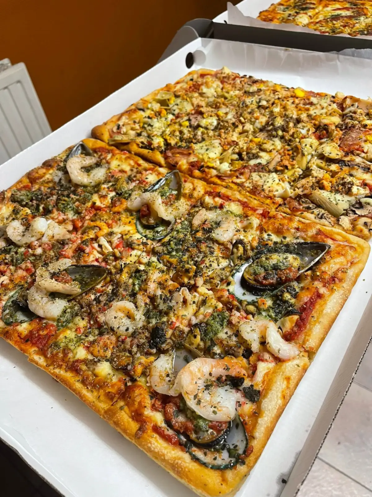 Une grande pizza rectangulaire découpée en parts, préparée pour un buffet.