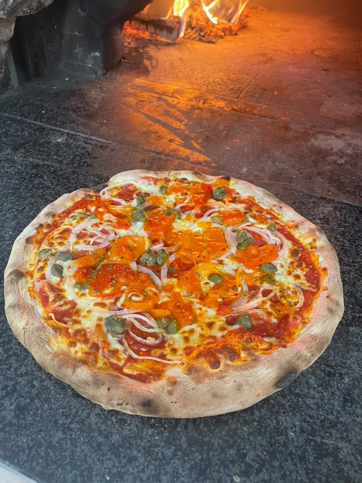 Une pizza aux tomates fraîches, olives et oignons rouges, sortie du four à bois.